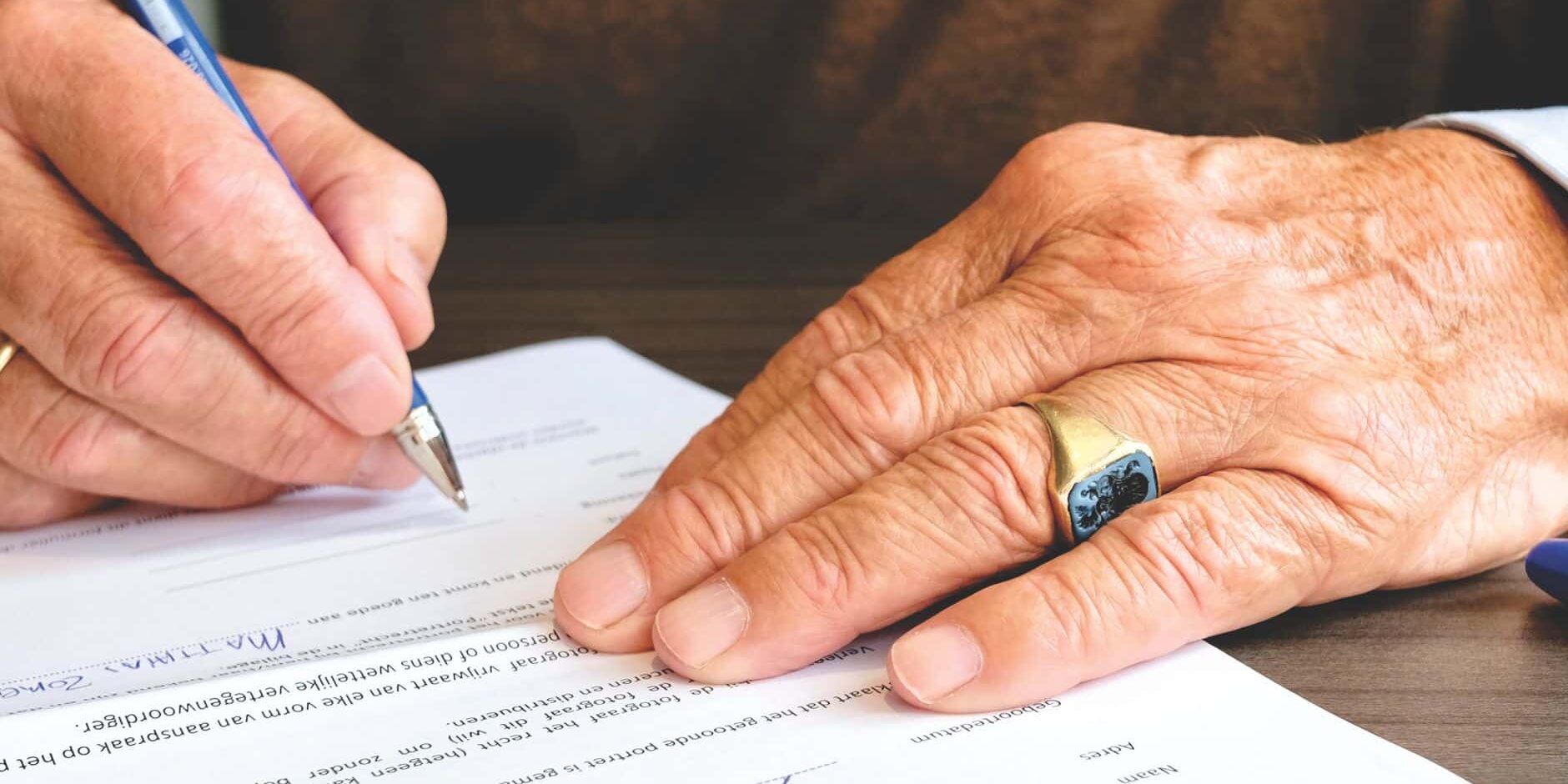Tramitar una herencia: firma de documentos de la testamentaría Persona mayor firmando un documento legal durante la tramitación de una herencia